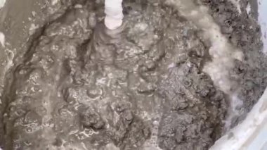 Bir mikserle inşaat karışımının hazırlanması. Çimento harcını elektrikli mikserle karıştırmak yakın plan, karışık havan topu deseni. İnşaatta el işçiliğinin otomasyonu..
