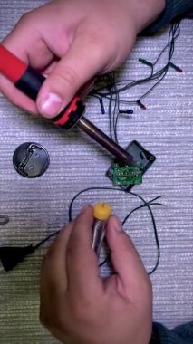 Elektrikli lehimleme demiriyle bir adamın ellerine yakın çekim. Tamirci, elektrik çelenginde röle yapar. Bir adam Noel tatili için evini dekore etmek için çelenk hazırlıyor..