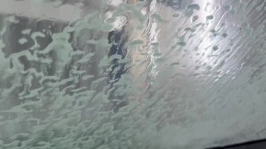 Ön camdaki köpüğü yıkayan su basıncının makro görüntüsü. Otomatik oto yıkama kabini görüntüsü.