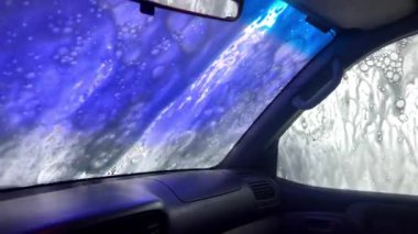 Robot oto yıkama, otomatik köpüklü araba yıkama sistemi. Bir arabayı sabunlarken çekilmiş renkli kısa bir video. Sabun solüsyonu. Araba camında beyaz köpük deterjanı var..