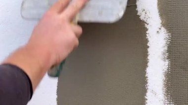 Ev yalıtımı için ağ ve sert poliüretan köpüğü takviyesine havan topu uygulayan bir malayla işçi elinin yakın çekimi. Metal bir spatula ile çalışan bir işçi sıva. Duvarların yalıtımı. Dış