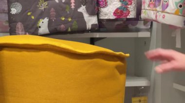 Dişi el, sarı puf testi yapıyor. Ev yapımı tekstil bölümünden bir kadın sarı fasulye torbası sandalyesini inceliyor. Eller kapalı, arka plan bulanık. İç ögeleri seçmek ve satın almak için fikirler