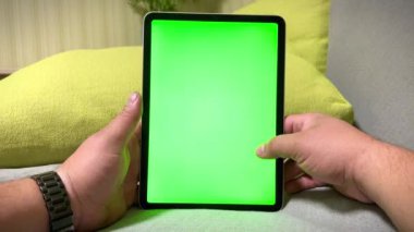 Bir adam elinde boş yeşil ekranlı dijital bir tablet tutuyor. Bir adam evde rahatlıyor, bilgisayar oyunları oynuyor ve bir web sitesine göz atıyor. Krom anahtarlı video şablonu. Kromakey ekran -