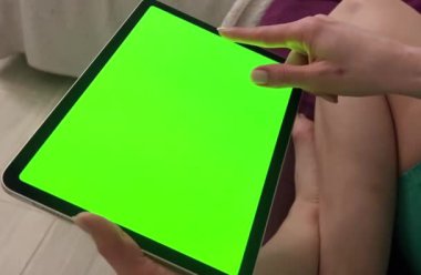 Bir kızın ellerinde yeşil ekran klavyeli dijital tablet. Evde bir kız çevrimiçi bir mağazadan hediye sipariş ediyor. Lotus pozisyonundaki bir kadın bir gezi turu seçer. Yeşil Ekran