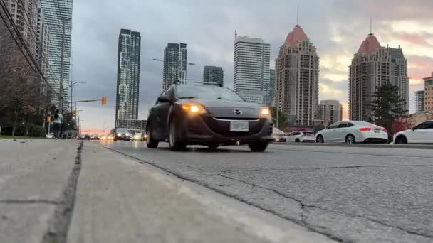 カナダ ミサウガ28 イブニングシティ 現代都市の風景 日没に近代的な都市 ひび割れた道路の表面 ベビーカーを持った女性 ライトがついている車の流れ シティロード — ストック動画