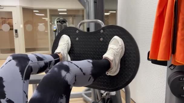 Γυναίκα Στο Γυμναστήριο Εκτελεί Μια Άσκηση Πόδι Τύπου Σχετικά Συσκευή — Αρχείο Βίντεο