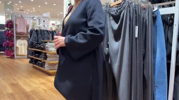 カナダ ミッサウガ 女性は衣料品店で服を選択します 鏡の前にいる女性が セールスフロアの青い暖かいカーディガンを試している — ストック動画