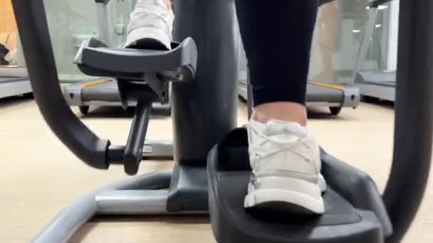 カナダのミシサガ Gymについて ジムにいる女性はスポーツマシンに乗っている カーディオ ロード 花の女性の足の後ろのビュー 健康的なライフスタイルのコンセプト — ストック動画