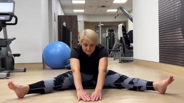 カナダのミシサガ ストレッチ 高齢の女性はフィットネスセンターの床に座っている間 運動を伸ばします 太りすぎの女性は健康のための腕と脚の筋肉を伸ばします — ストック動画