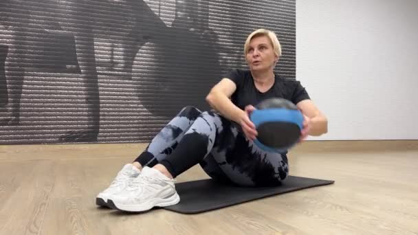 女性はフィットボールで腹部運動を行います 強度の構築と柔軟性のための機器を備えた屋内でのフィットネストレーニング — ストック動画