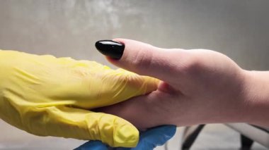 Tırnak teknisyeninin eldiven giyip müşterilerinin elini tutmasına yakın çekim. Siyah manikür, müşterilerin el ve manikürcülerinin yakın çekim videosu. Manikürcüye kabuk bağlamak.