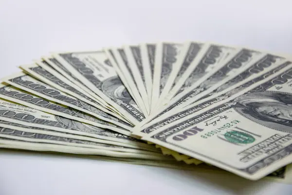 stock image A closeup shot of a stack of new, hundred-dollar bills fanned out on a plain white background.