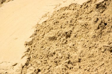 Açık kahverengi kum yığınının yakın çekim görüntüsü, güneşli bir günde muhtemelen açık havada çekilmiş. Kum kuru ve gevşek görünüyor, kaba bir dokusu var..