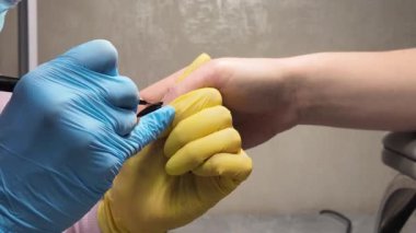 Bir manikürcünün işi. Lastik eldivenli manikürcü beyaz bir kadının elinin tırnağına siyah Shellac jel cilası sürmüş. Yakın çekim video. Manikürcüde sağlık hizmeti, kozmetik spa prosedürü.
