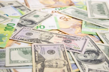 Beyaz bir yüzeye serpilmiş Amerikan dolarları ve Euro banknotları.
