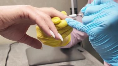 Manikür salonu. Manikürcünün profesyonel el hareketleri. Bir kat jöle cilasını çıkarırken çekilmiş detaylı bir video. Sarı ve mavi eldivenli şık bir manikürcü. Güzellik endüstrisi, tıp ve güzellik.