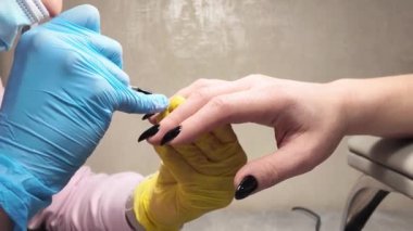 Manikür. Manikürcünün elinde bir kadın eli. Uzun tırnaklara siyah cila uygulanıyor.