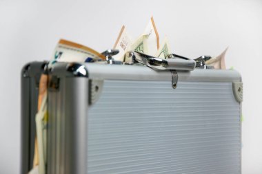 Banknotlarla dolu gümüş bir çanta beyaz bir arka planda duruyor..