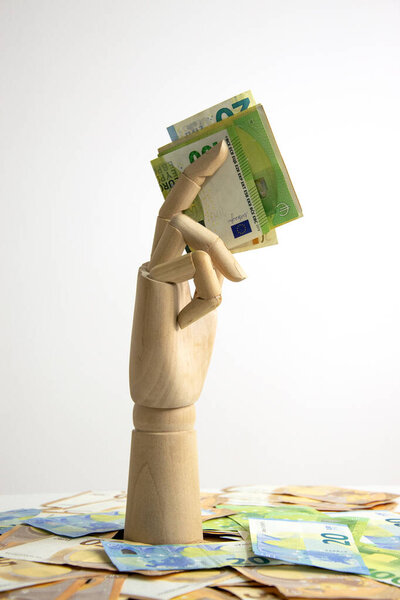 Деревянная рука с пачкой банкнот евро появляется из кучи банкнот евро на белом фоне.