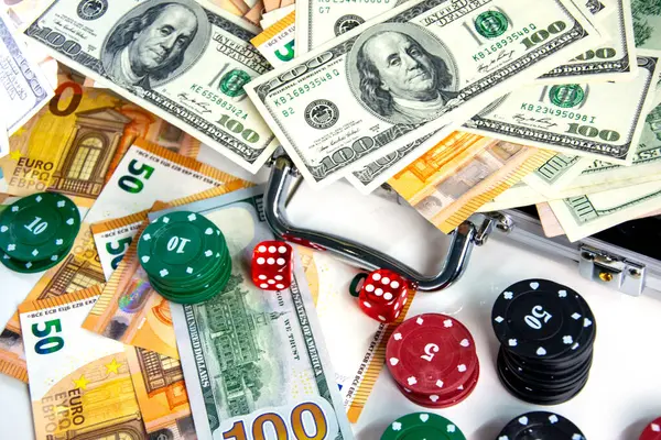 stock image A close-up image of various poker chips, dice, and US dollar bills and Euro banknotes scattered on a white surface.