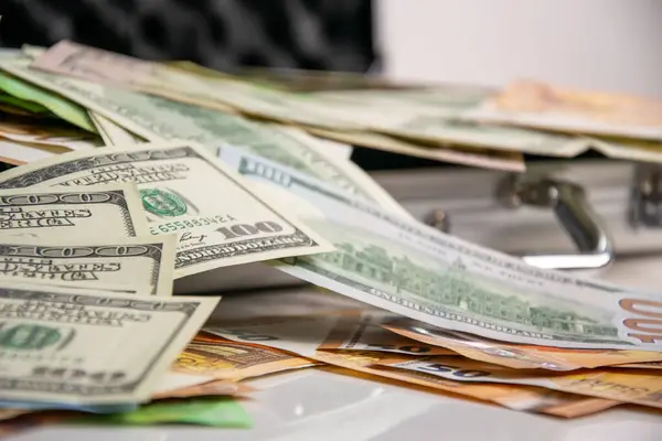 Üstünde 100 dolarlık banknotlar olan bir yığın gümüş bir kutunun üzerinde duruyor..