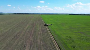 Geniş tarım arazileri yeşil ve kahverengi alanları zıt gösteriyor. Tarım ekipmanları açık mavi bir gökyüzünün altında tüylü bulutlarla aktif olarak çalışabilir..