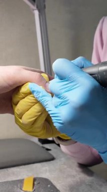 Bir kadın bir kozmetikçiden manikür yaptırıyor. El bakımı süreci yakın çekim. Donanım manikürünün dikey videosu. Kozmetik ve tıp. Dikey video. Konsept: Profesyonel tırnak bakımı