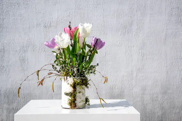 Mor ve beyaz tonlarında renkli laleler dokulu bir vazodan çiçek açar ve minimalist bir ortama tazelik katar..