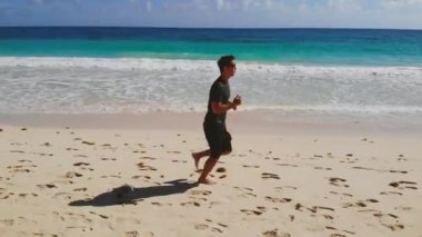 Fitness Adam Koşucusu. Yetişkin, zayıf, atletik bir adam deniz kıyısında kumda yalınayak koşar. Okyanusun kıyı şeridi boyunca spor koşusu. Doğada deniz manzarasında koşan atletik koşucu.