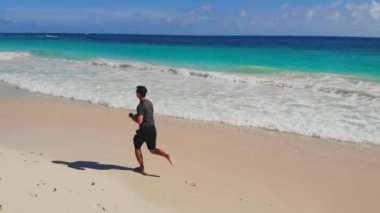 Fitness man running jog on morning at sea. Adult slim, athletic, fit man runs barefoot along coast of sea on sand. Sports jogging on vacation along coastline of ocean. Healthy lifestyle in clean air.