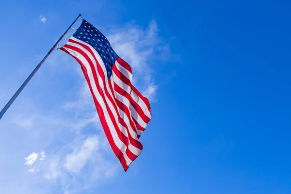 Close up of large American flag waving in front of blue sky and white cloud. American Flag waving in wind. Close up of United States flag. American Flag Waving Under A Blue Sky With Clouds.