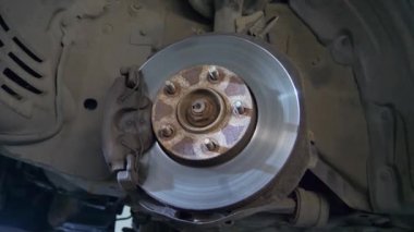 Car Wheel Hub Fren Diski ile, fren diskini incele, arabanın üstünde kalibreli, alt görüşlü. Bir araba tamirhanesinde fren diskini tamir ediyorum. Eski paslı fren diski yakın plan. Araba tekerleğinin paslı merkezi.