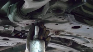 Close up unscrewing car bolts. Dirty hands of an auto mechanic unscrew bolts on bottom of car, close-up. Male mechanic unscrew automobile detail of running gear of car. Car suspension repair.
