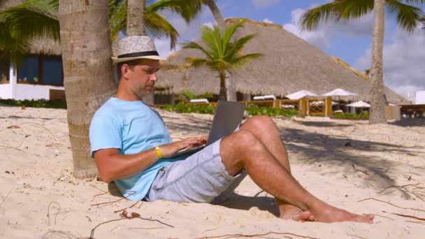 带着笔记本在沙滩上放风 在棕榈树下的海滩上工作的自由职业者 自由职业者完成工作 关闭他的笔记本电脑 并退出框架 工作和假期 自由职业旅行概念 — 图库视频影像