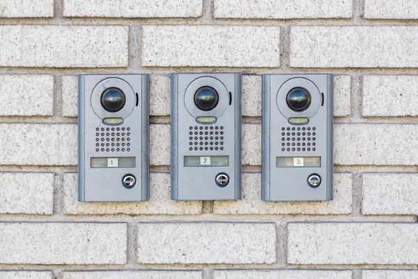 Three intercom on white textured brick wall, Close up. Apartment numbers and push button door buzzer. House intercom doorbell entrance home with a surveillance camera. Intercom doorbell on building