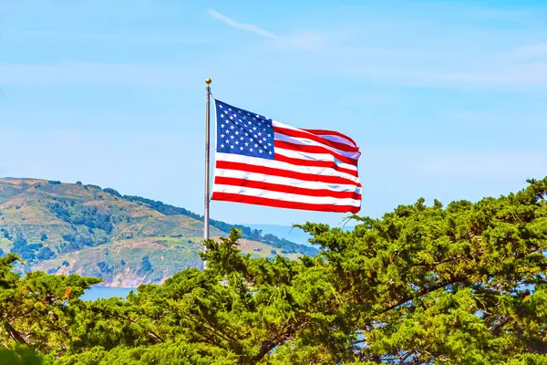Rüzgarda dalgalanan Amerikan bayrağı, arka plandaki dağlar ve ağaçlar. Dağlara tepeden bakan Amerikan Bayrağı ağaçlara ve dağlara tepeden bakıyor. San Francisco 'da Amerikan bayrağı
