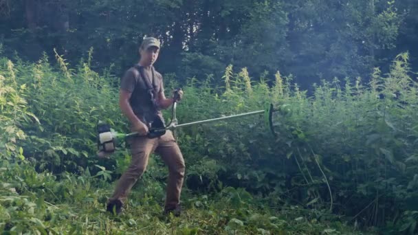 年轻的园丁在割草的同时 用汽油割草机玩电吉他 快乐的人在花园里享受时光 感觉像摇滚明星 看着相机 — 图库视频影像