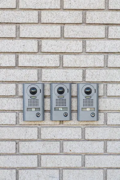Three modern intercom on white wall near entrance to the house, space for text. Outdoor Video Intercom Door Station on brick wall. Intercom with video communication in the brick wall for opening door