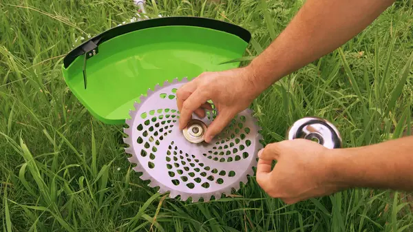 Installing a saw blade on a new green brush cutter. Gardener sets up a saw blade against a grassy field, close up. Preparing the brush cutter for work. Servicing garden tools.