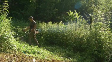 Manzara bakım konsepti. Bahçede çim biçme makinesi ve çim biçme makinesi kullanan bir adam. Bahçe işçisi çim biçiyor. Evin arka bahçesinde çim biçme makinesi olan genç bahçıvan.