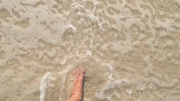 海岸の砂の上を歩くトップビューの足 オスの足は海の近くを歩く 波で砂浜に行く男の裸の足 夏休みや休日アップPovを閉じます 動画をスライドさせる — ストック動画