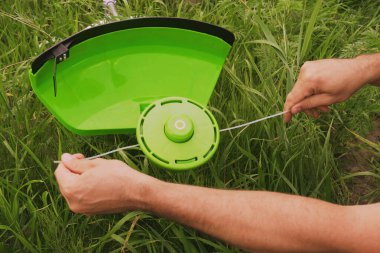 Bahçe aletlerine bakıyorum. Bahçıvan çayırdaki çim biçme makinesine makara takıyor. Parçaları değiştirmek için çim biçme makinesini parçalayan bir adamın yakın çekimi. Bobini çim biçme makinesine yerleştiriyorum.