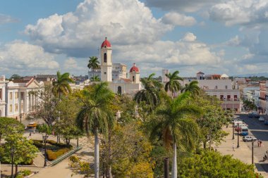 CIENFUEGOS, CUBA - 13 Ocak 2022 - Kusursuz Gebeliğin Katedrali. 2005 yılında Cienfuegos UNESCO 'nun Dünya Mirası listesine girdi. Eski kasabanın arka planında kilise kulesi olan palmiye ağaçları.