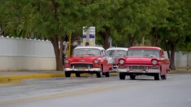 Varadero, Küba - 15 Ocak 2022 - Antika kırmızı retro arabalar yağmurlu bir günde Küba tatil köyünün merkez caddesi boyunca sürüyorlar. Küba 'da bir tatil köyünde kırmızı bir taksi yol boyunca ilerliyor. Küba 'da eski bir taksinin yanında turistler