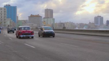 Havana, Küba - 10 Ocak 2022 - Arka planda okyanus olan malecon üzerinde giden klasik arabalar. Kış fırtınası sırasında Havana Küba 'da Malecon' da dalgalar kopar. Denize yakın bir şehir manzarası ve yolda çalışan bir araba.