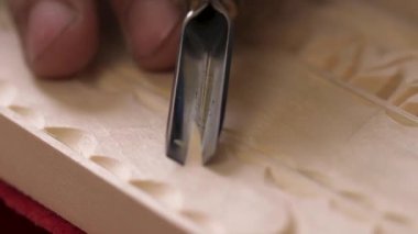 Tahta oyma. Kutu oyma işlemi. Marangoz odun keskisiyle bir süs çıkarır, talaşları fırçalar. El yapımı ahşap işçiliği. Keskiyle odun oymanın ayrıntıları. Düşük odak derinliği, süper makro çekim