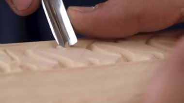 Marangoz odun keskisiyle bir süs çıkarır, talaşları fırçalar. El yapımı ahşap işçiliği. Keskiyle odun oymanın ayrıntıları. Düşük odaklanma derinliği, süper makro çekim. Tahta oyma. Oyma kutusu işlemi