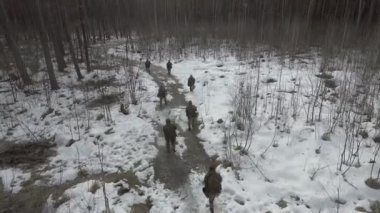 Kamuflaj üniformalı tam teçhizatlı askerlerden oluşan bir grup, saldırı tüfekleri ile donatılmış makineli tüfekler, kışın askeri keşif sırasında yoğun orman boyunca terk edilmiş bir yolda ilerliyorlar.