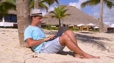 Serbest meslek kavramı. Yakışıklı, başarılı bir genç okyanus kıyısında dizüstü bilgisayarla uzaktan sörf yapıyor. İşadamı serbest programlama çevrimiçi metin yazarı, cennet manzarası, rüya işi