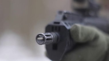 Asker kalimasyon gözünden ileri doğru makineli tüfek, ön görüş, sığ alan derinliği. Makineli tüfeğin namlusu yakın plan, bir adamın bulanık arka planı. Askeri çatışma. Askeri operasyon.